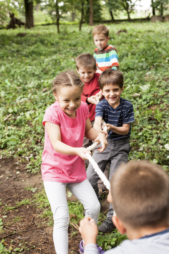 Eine Gruppe lachender Kinder spielt Tauziehen auf einer grünen Wiese.