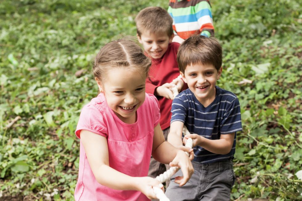 Eine Gruppe lachender Kinder spielt Tauziehen auf einer grünen Wiese.